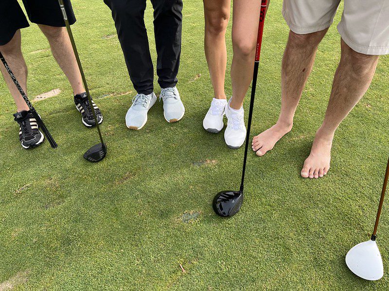 Four golfers' feet and clubs on golf green