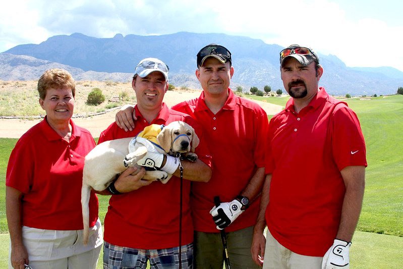 Four golfers in red shirts holding puppy